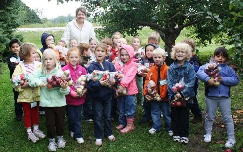 School group holding bags of freshly picked apples in the orchard